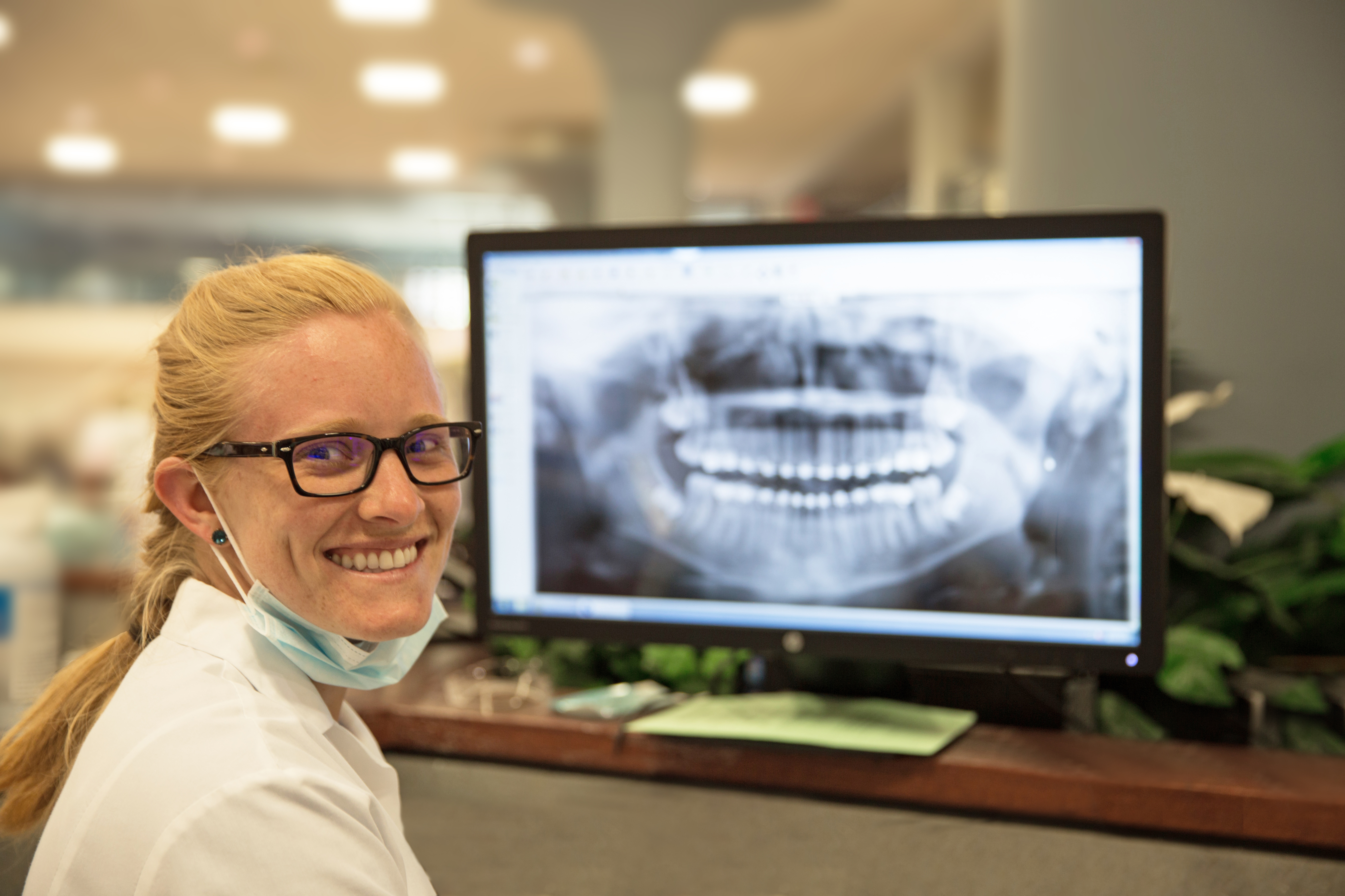 Female orthodontist looking over her shoulder, smiling, with an X-Ray on her computer screen.