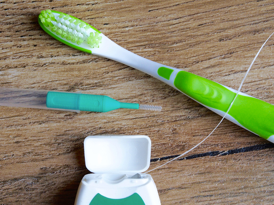 Dental floss, interdental brush and toothbrush on wood background