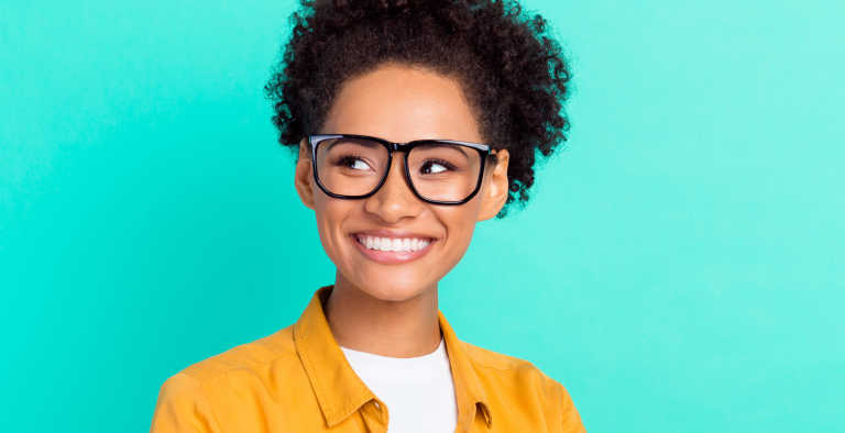 Middle aged black women wearing glasses and showing off her great smile on a teal background.