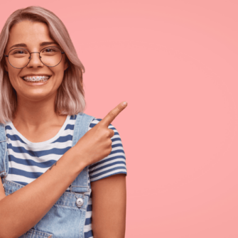 Teenage Girl on a pink background with braces, pointing at the important information of seeing an orthodontist.