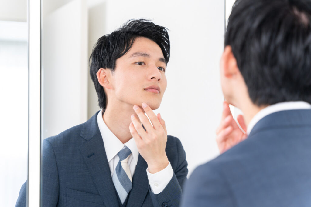 Man in a suit looking in the mirror at his jaw line.