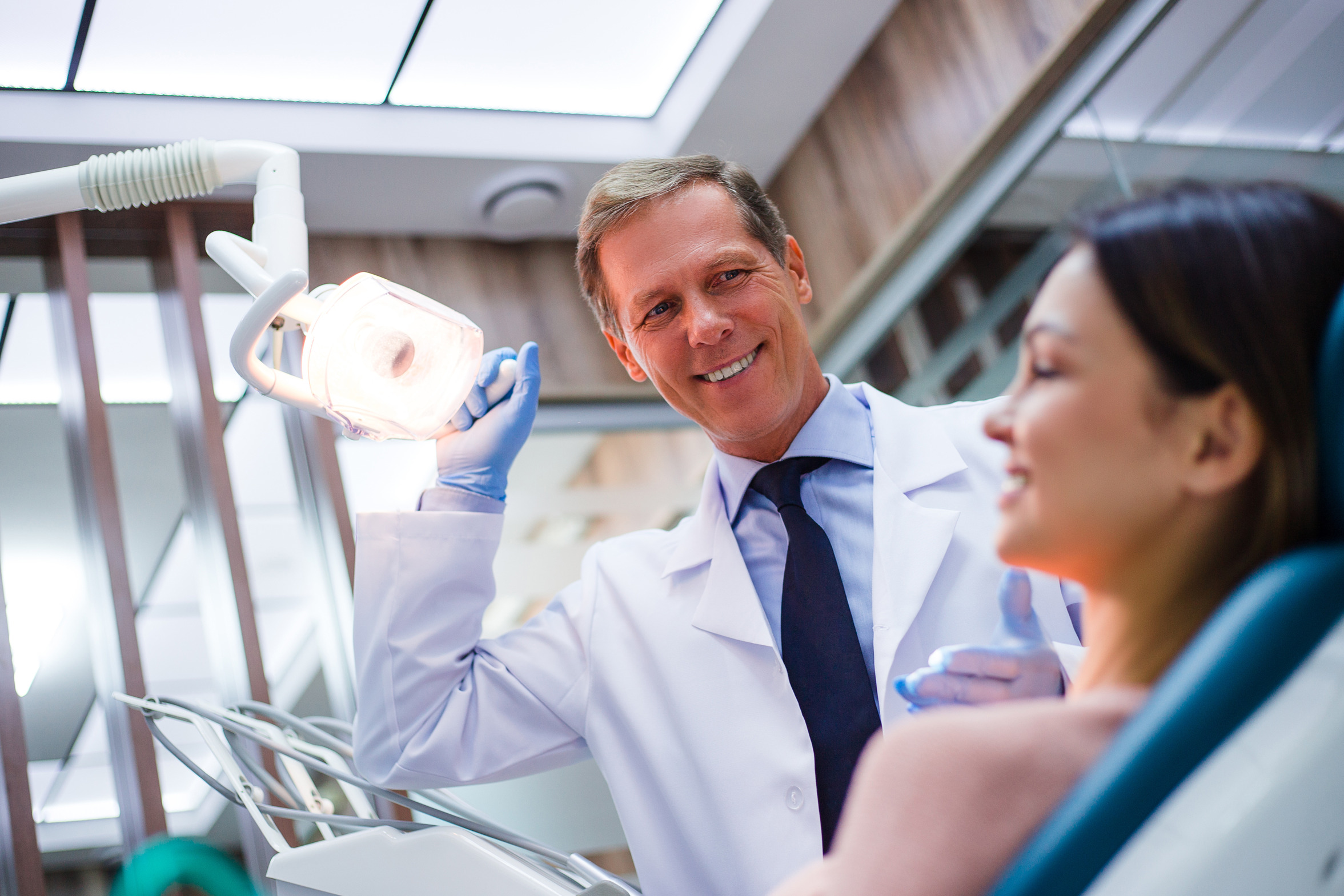 Orthodontist shining a light into a patients face, while they are sitting in a dental chair.